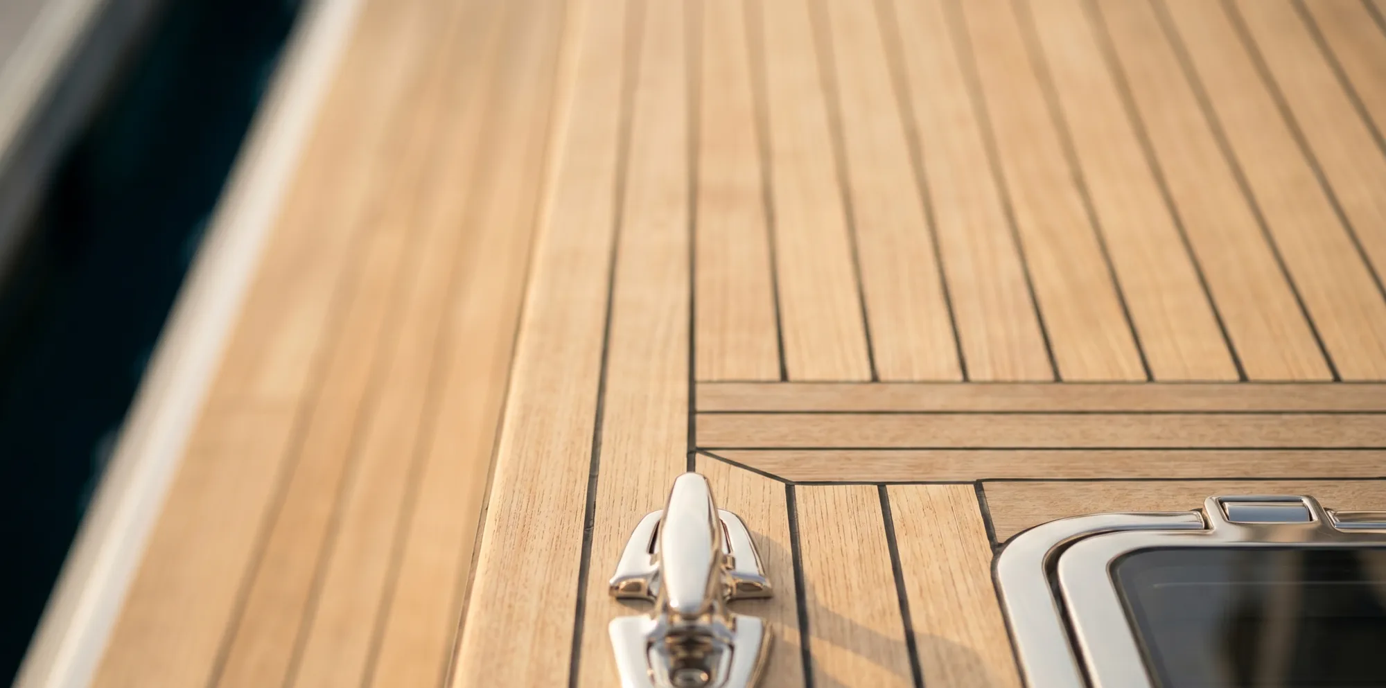 Sunlit teak deck planking with a polished stainless deck cleat