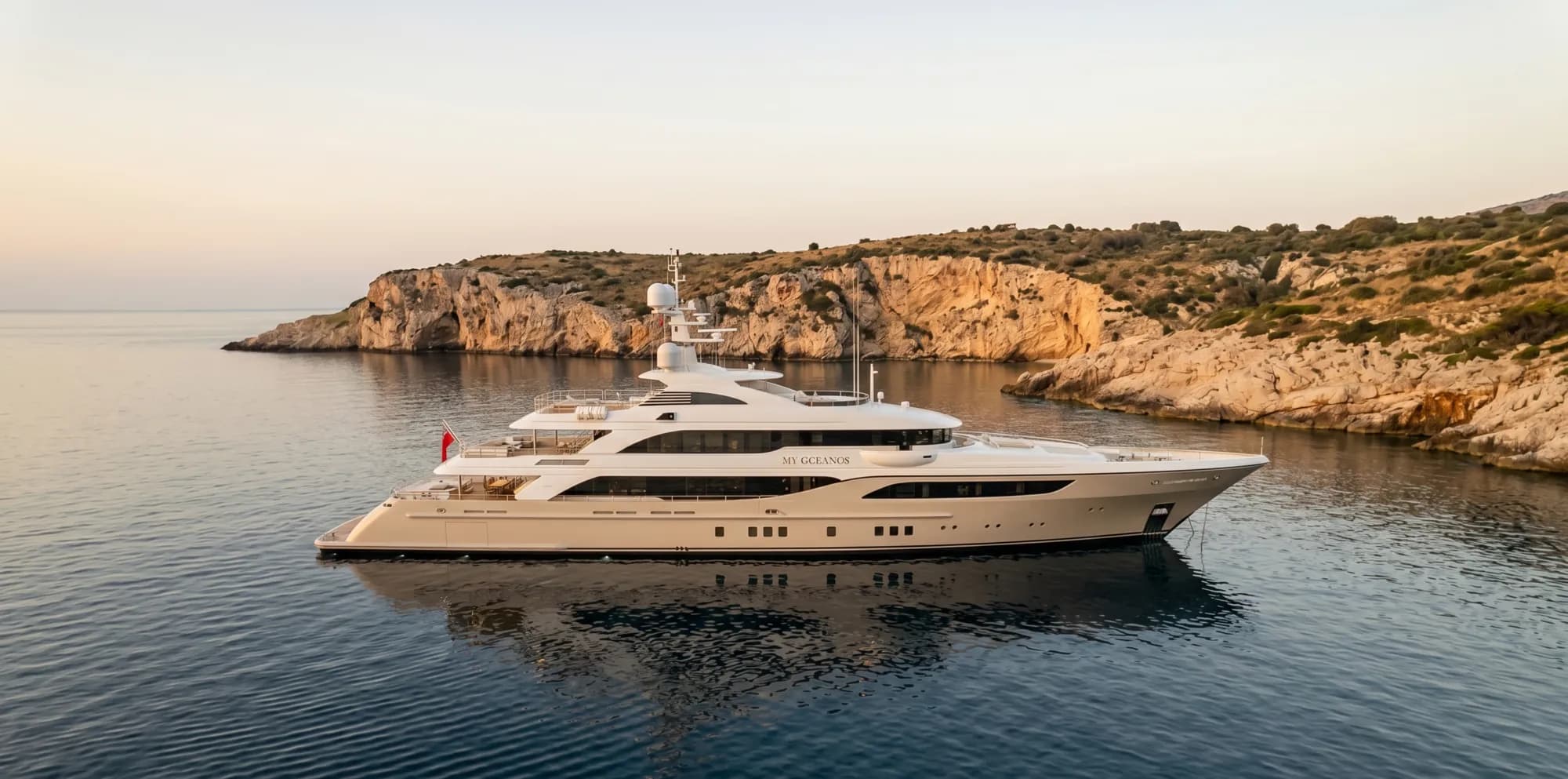 A white superyacht anchored at a headland at soft dusk